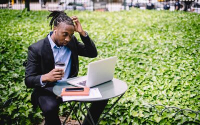 thoughtful young black man working on laptop in outdoor cafe and drinking coffee